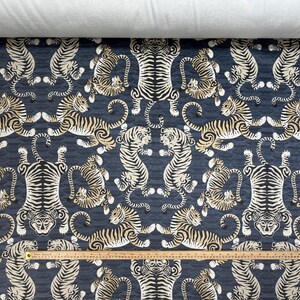 May include: Dark blue fabric with a repeating pattern of stylized tigers in cream and black. The tigers are arranged in various poses, creating a symmetrical design. A wooden ruler is placed across the bottom.
