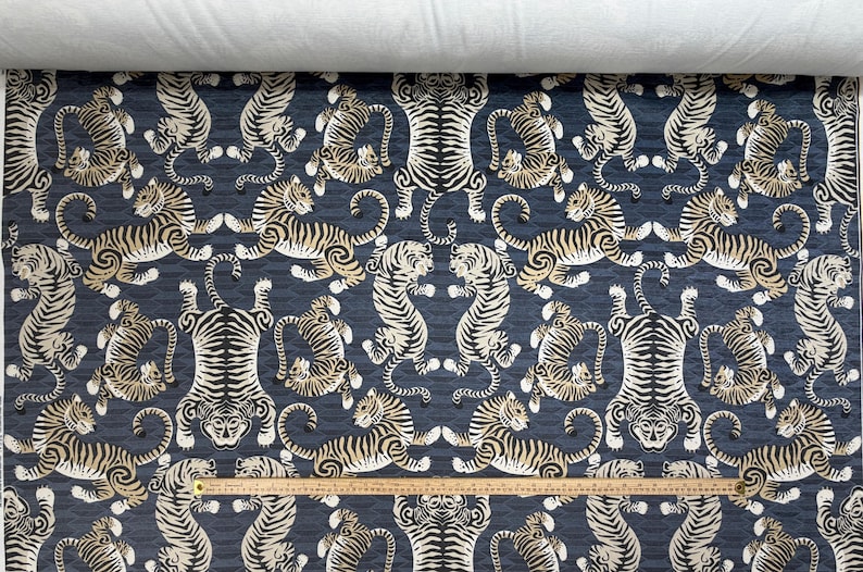 May include: Dark blue fabric with a repeating pattern of stylized tigers in cream and black. The tigers are arranged in various poses, creating a symmetrical design. A wooden ruler is placed across the bottom.