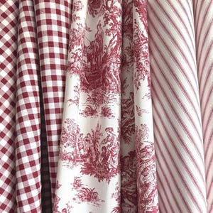 May include: Three rolls of fabric displayed side by side. The first roll features a red and white gingham check pattern. The second roll displays a red and white toile de jouy print with pastoral scenes. The third roll has a red and white diagonal stripe.