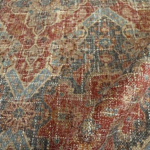 May include: Close-up of a red, blue and brown patterned fabric with a woven texture. The fabric has a traditional design with intricate details.