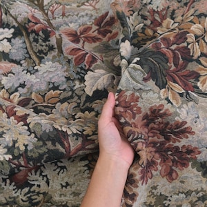 Hand holding heavyweight tapestry upholstery fabric in Woodrose foliage pattern, woven jacquard textile with scenic verdure design, antique style upholstery material perfect for sofas, armchairs, ottomans, curtains, wall hangings, and furniture restoration projects.