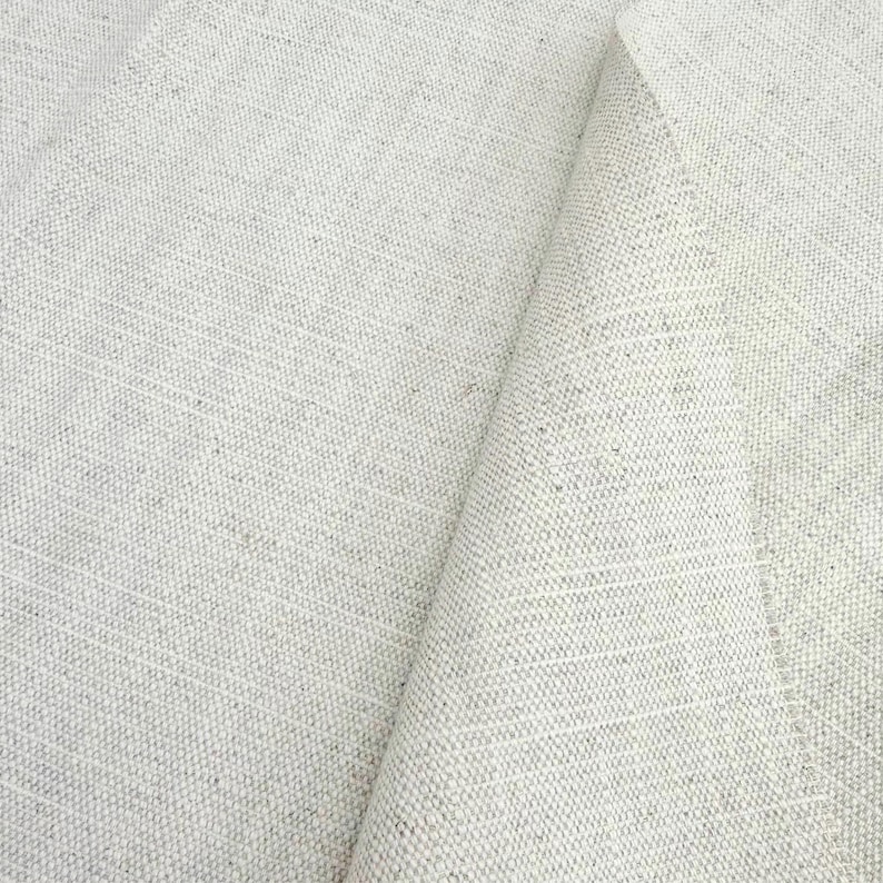 May include: A piece of off-white, natural-colored fabric with a visible, coarse woven texture. The material features a dense, uniform grid pattern with subtle flecks of darker beige and brown fibers throughout the weave, creating a neutral appearance.