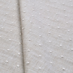 May include: A light beige fabric featuring a repeating pattern of small, raised white tufted dots arranged in vertical lines. The textile has a visible woven texture with a natural, neutral tone and a consistent grid of soft, textured embellishments.