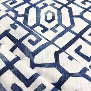 May include: A white fabric featuring a repeating dark blue geometric pattern with interconnected lines and angular shapes. The textile displays a visible woven texture with a slightly distressed, hand-painted appearance across the surface.
