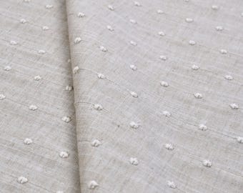 クリーム色のリネン生地に縦方向のドット刺繍を施した、ニュートラルなホームデコレーションテキスタイル。砂色の亜麻の斑点模様、繊細なパール柄、軽やかでシックなスタイル、モダン。