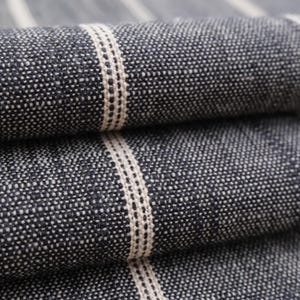May include: Close-up of folded fabric with a textured, speckled appearance. The fabric is primarily dark blue with vertical stripes of off-white. The stripes are centered with a dotted pattern. The fabric appears to be woven.