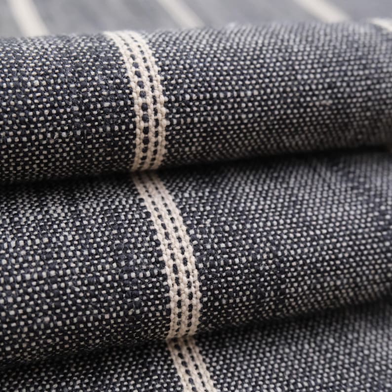 May include: Close-up of folded fabric with a textured, speckled appearance. The fabric is primarily dark blue with vertical stripes of off-white. The stripes are centered with a dotted pattern. The fabric appears to be woven.