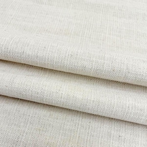 May include: A light beige fabric with a visible woven texture and subtle vertical stripes. The material features a natural, speckled appearance with a consistent weave pattern throughout, showing folds that create soft shadows across the surface.