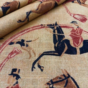May include: Tan fabric with a repeating pattern of polo players on horseback. The design features riders in red and brown attire, with black horses and a red and brown circular border. The fabric has a textured appearance.