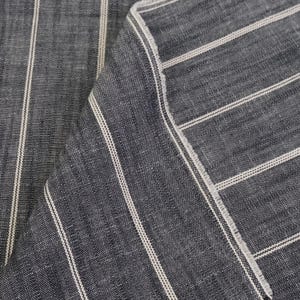 May include: Close-up of a folded piece of fabric. The fabric is a dark blue with vertical white stripes. The edges of the fabric are frayed, showing the texture and weave of the material.