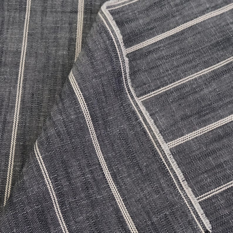 May include: Close-up of a folded piece of fabric. The fabric is a dark blue with vertical white stripes. The edges of the fabric are frayed, showing the texture and weave of the material.