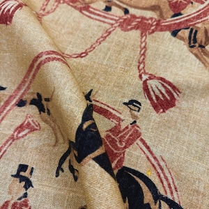 May include: Tan fabric with a repeating pattern of riders on horseback, depicted in red, brown, and black. The design includes ropes, tassels, and musical instruments, creating a vintage equestrian theme.