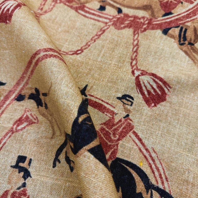 May include: Tan fabric with a repeating pattern of riders on horseback, depicted in red, brown, and black. The design includes ropes, tassels, and musical instruments, creating a vintage equestrian theme.