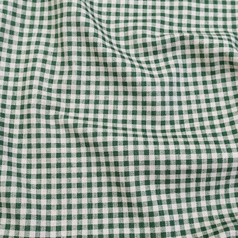 May include: A fabric featuring a classic gingham pattern with a repeating grid of dark forest green and white squares. The material displays soft folds and natural draping, highlighting the consistent woven texture of the checkered textile design.