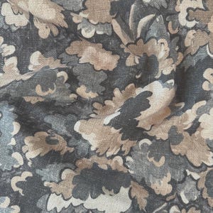 May include: Close-up of a fabric with a floral pattern. The design features overlapping, stylized flowers in shades of gray, brown, and beige. The fabric has a slightly wrinkled texture, suggesting it may be a soft material like silk or linen.
