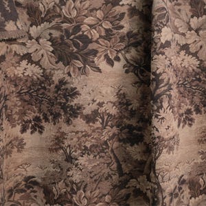 May include: Close-up of a fabric with a detailed forest scene in shades of brown, beige, and dark gray. The design features trees, foliage, and leaves, creating a textured, naturalistic pattern. The fabric has a slightly rough texture.