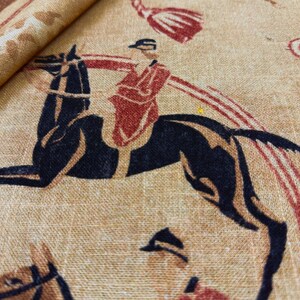 May include: Tan fabric with a repeating pattern of riders on black horses. The riders are wearing red jackets and black caps. The fabric also features red and brown decorative elements.