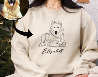 May include: A cream-colored sweatshirt featuring a line drawing of a dog, with the name "Elizabeth" below. A photo of a similar dog is in a circle above the drawing. The sweatshirt is part of a pet-themed collection.