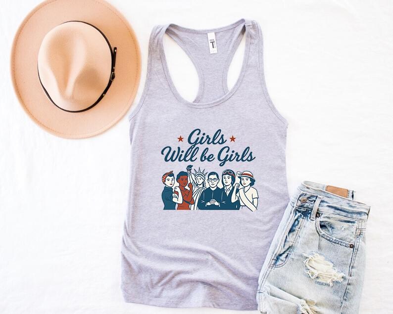 Pode incluir: Uma regata cinza claro com o texto "Girls Will be Girls" e uma ilustra&ccedil;&atilde;o de v&aacute;rias mulheres. Um chap&eacute;u bege com uma faixa preta e um par de jeans de lavagem clara tamb&eacute;m est&atilde;o na imagem.