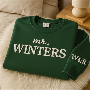 May include: A dark green sweatshirt with the text "mr. WINTERS" in white, stylized lettering across the chest. The sleeve cuff displays the initials "W&R" in white. The sweatshirt is made of a soft material.
