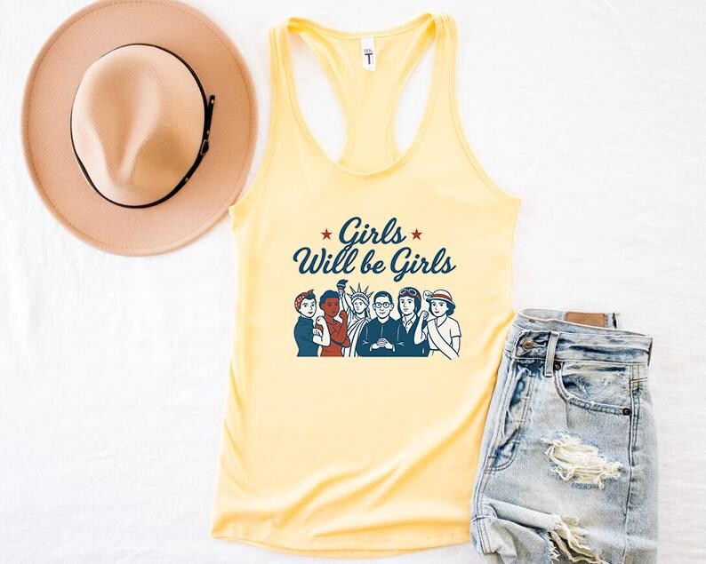 Pode incluir: Uma regata amarelo claro com o texto "Girls Will be Girls" em escrita azul marinho e um gr&aacute;fico de mulheres diversas. Um chap&eacute;u bege com uma faixa preta e jeans azul claro tamb&eacute;m est&atilde;o na imagem.