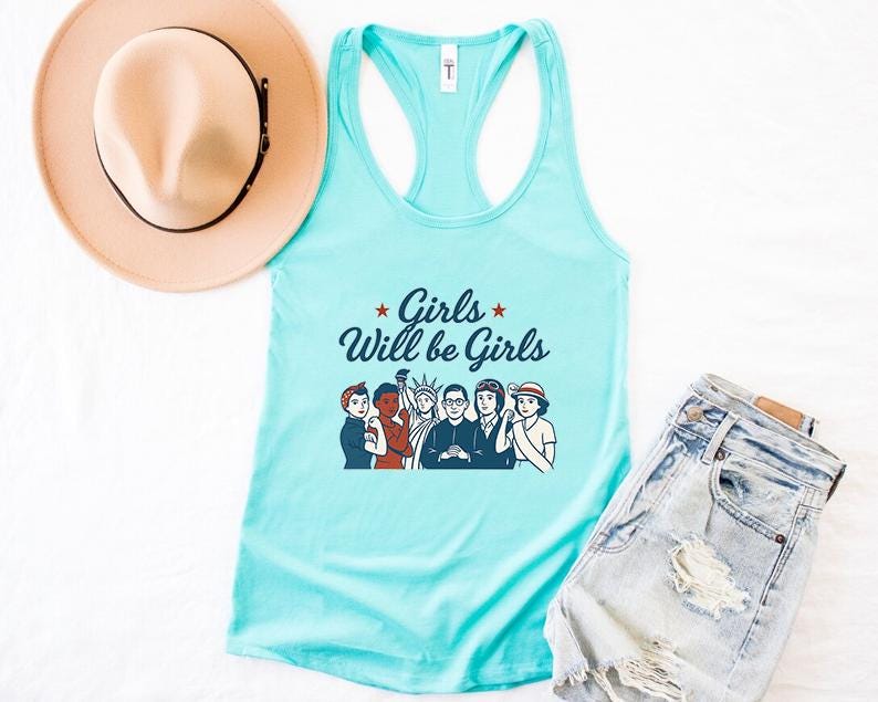 Pode incluir: Uma regata azul clara com o texto "Girls Will be Girls" e um gr&aacute;fico de mulheres. Um chap&eacute;u bege com uma faixa preta e cal&ccedil;&otilde;es de ganga tamb&eacute;m s&atilde;o vis&iacute;veis.