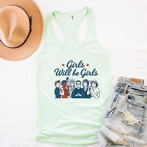 Pode incluir: Uma regata verde claro com o texto "Girls Will be Girls" e um gr&aacute;fico de seis mulheres. A regata &eacute; combinada com shorts jeans e um chap&eacute;u bege.