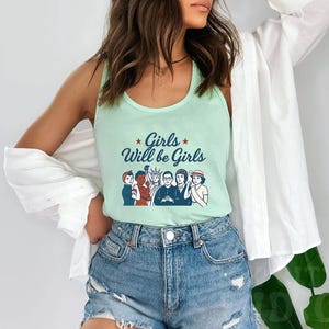 Pode incluir: Uma regata verde clara com o texto "Girls Will be Girls" e um gr&aacute;fico de seis pessoas. A regata &eacute; combinada com shorts jeans. O estilo geral &eacute; casual e confort&aacute;vel.