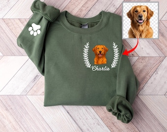 May include: Olive green sweatshirt featuring a golden retriever illustration within a white laurel wreath. The name "Charlie" is printed below the dog. A white paw print is on the left sleeve. The image includes a separate photo of the dog.