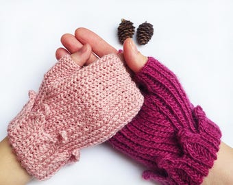 May include: A pair of fingerless gloves, one pink and one burgundy, with a knitted texture. The gloves have a decorative detail on the cuff.