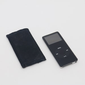 Op de afbeelding: Een zwarte iPod met een klein scherm en een ronde bedieningsknop met het woord "MENU" erboven. De iPod ligt op een wit oppervlak naast een zwarte draagtas.