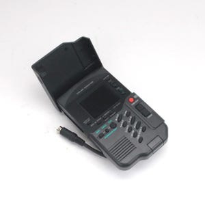 May include: A black portable colour monitor with a flip-up screen cover. The device features a small display, a red start/stop button, a zoom toggle, and various playback control buttons labelled with text including monitor on/off and data on screen.