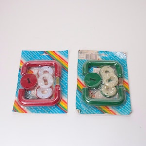 May include: Two sets of door handle hardware in sealed plastic packaging. One set features a red handle and red circular escutcheon, while the other has a green handle and green escutcheon. Both include white circular components and metal screws.