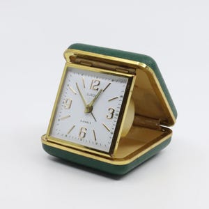 May include: A green leather travel alarm clock with a white face and gold hands. The clock face says "Euros" and "2 Jewels".