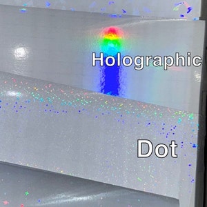K&ouml;nnte beinhalten: Nahaufnahme von vier verschiedenen Arten von wei&szlig;em, irisierendem Bastelvinyl. Die oberste Schicht ist mit "Gem" beschriftet, gefolgt von "Holographic", "Dot" und "Star". Jeder Vinyltyp hat einen einzigartigen Glitzer- oder Hologrammeffekt.