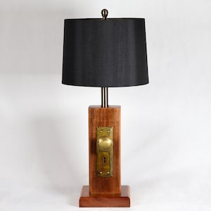 May include: A unique table lamp with a black lampshade, brass accents, and a wooden base. The lamp features a vintage brass doorknob and plate on the wooden column. The lamp is approximately 28 inches tall.
