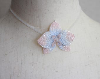 May include: A delicate white and pink beaded flower necklace. The flower is made of small beads and has a delicate, feminine look.