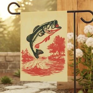 May include: A beige garden flag featuring a leaping bass fish illustration in black and red. The design includes a red river scene with trees. The flag is displayed on a black metal stand, suitable for outdoor decor.