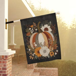 May include: A decorative outdoor flag featuring a large pumpkin design with orange, white, and gray stripes, surrounded by fall foliage and flowers. The flag is mounted on a white pole and displays against a dark background.