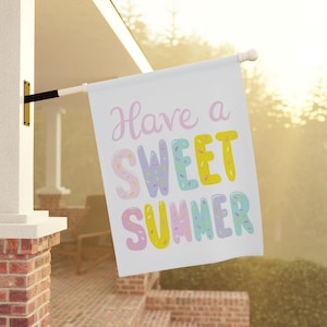 May include: White flag with the text "Have a SWEET SUMMER" in pastel colors. The word "SWEET" has a sprinkle design. The flag is hanging outside on a sunny day.