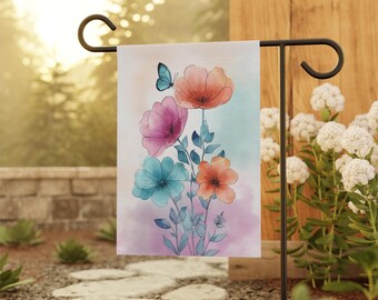 Puede incluir: Una bandera de jardín con un diseño floral en acuarela. Presenta flores naranjas, rosas y turquesas, y una mariposa azul. La bandera está montada en un poste de jardín de metal negro, ideal para la decoración exterior.