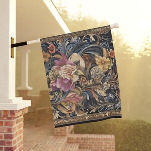 May include: A decorative outdoor flag featuring a floral design with pink, yellow, and blue flowers on a dark background. The flag has a detailed border and is mounted on a white pole.