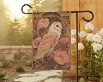 Puede incluir: Bandera de jardín con ilustración de búho. El búho tiene cara blanca y plumas marrón rosado, rodeado de flores y follaje rosa. La bandera se muestra en un soporte de metal negro, en un entorno de jardín.