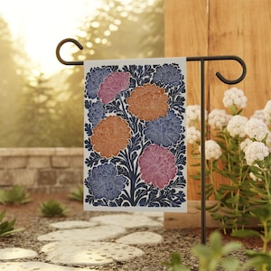 May include: A rectangular garden flag featuring a floral design with orange, pink, and blue flowers on a white background. The flowers are set against a dark blue leafy background. The flag is displayed on a black metal garden flag holder.