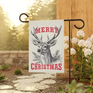May include: A cream-colored garden flag with a vintage illustration of a deer head and antlers. The words "MERRY CHRISTMAS" are printed in red. The flag is displayed on a black metal garden stake.
