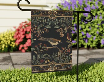 May include: A decorative garden flag featuring a detailed illustration of a bird perched on a branch, set against a dark background with floral and foliage elements. The flag is displayed on a black metal stand, suitable for outdoor use.