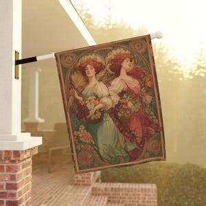 May include: An outdoor flag with an Art Nouveau design. It depicts two women with red hair, carrying baskets of fruit and wheat. The flag has a detailed border with floral and geometric patterns. It is mounted on a white pole.