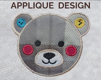 May include: Embroidered teddy bear applique design. The bear's head is gray with a plaid pattern, featuring button ears, pink cheeks, and a black nose and eyes. The text "TEDDY BEAR APPLIQUE DESIGN" is above the bear.