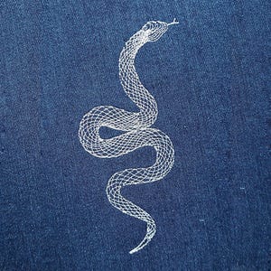 Könnte beinhalten: Weiß gesticktes Schlangenmuster auf einem dunkelblauen Jeansstoff.