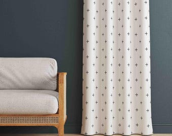May include: A floor-length curtain featuring a white fabric base with a repeating pattern of small black plus signs. The curtain hangs in vertical folds, displaying a consistent grid-like arrangement of the dark symbols across the light surface.